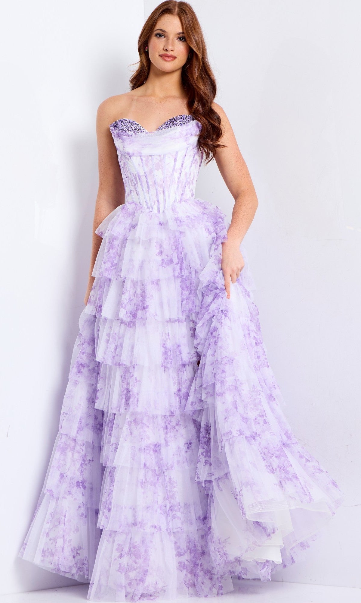 A woman wearing the Jovani 47440 long prom dress in lilac, featuring a strapless corset bodice, floral print, and tiered ruffle skirt, stands against a plain white background.